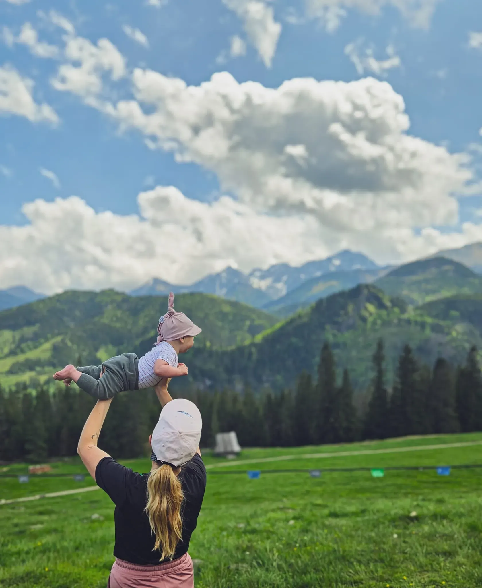 Mama unosi niemowlę na polanie z widokiem na Tatry